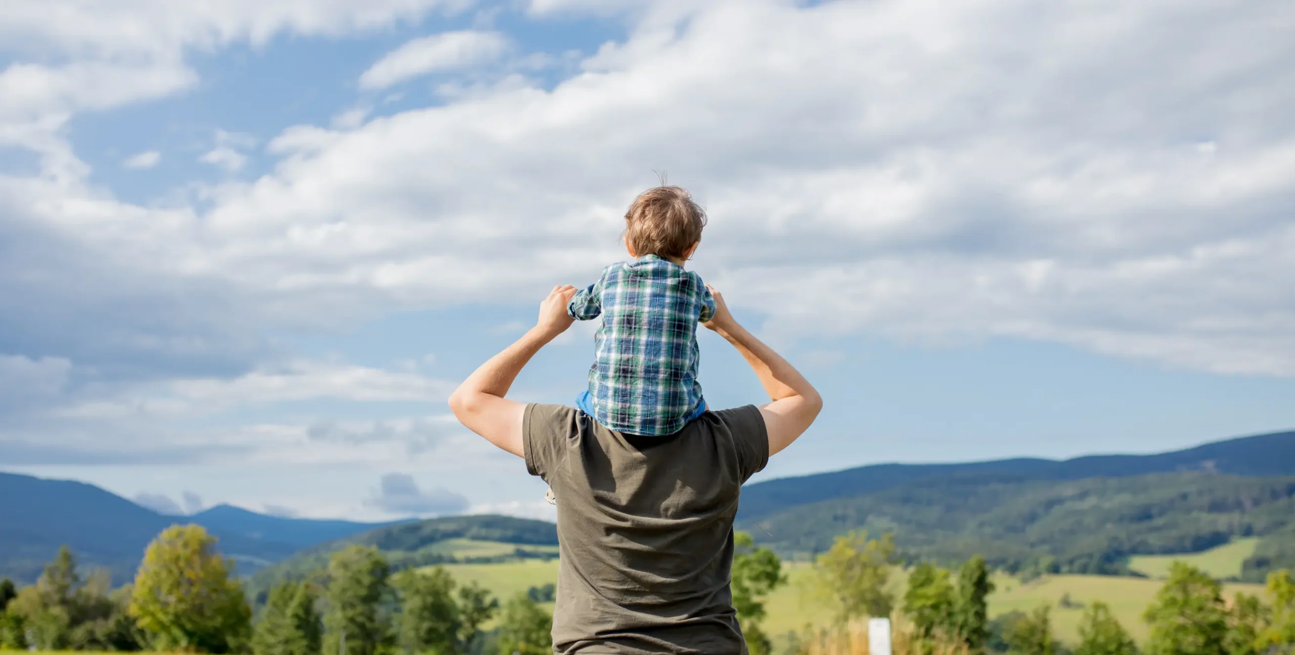 Un niño encima de los hombros de su padre mirando la montaña